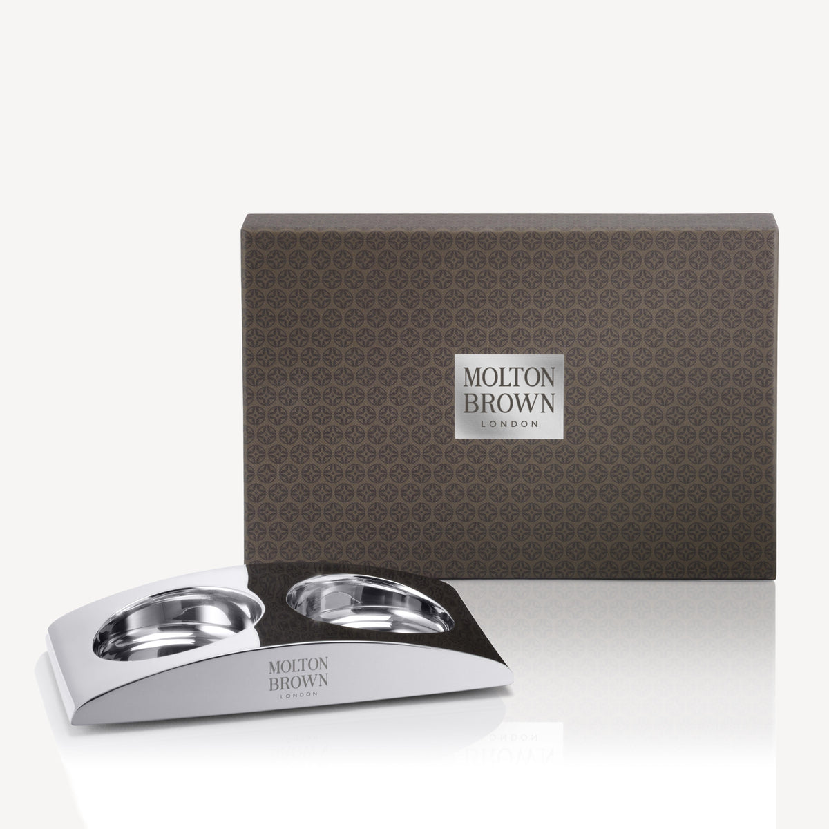 Introducing The Elemental Arc by MoltonBrown Cyprus: a gift set that includes a stainless steel hand wash holder with two round slots, presented in an elegant brown box featuring a subtle geometric pattern and the iconic Molton Brown London emblem at its center.