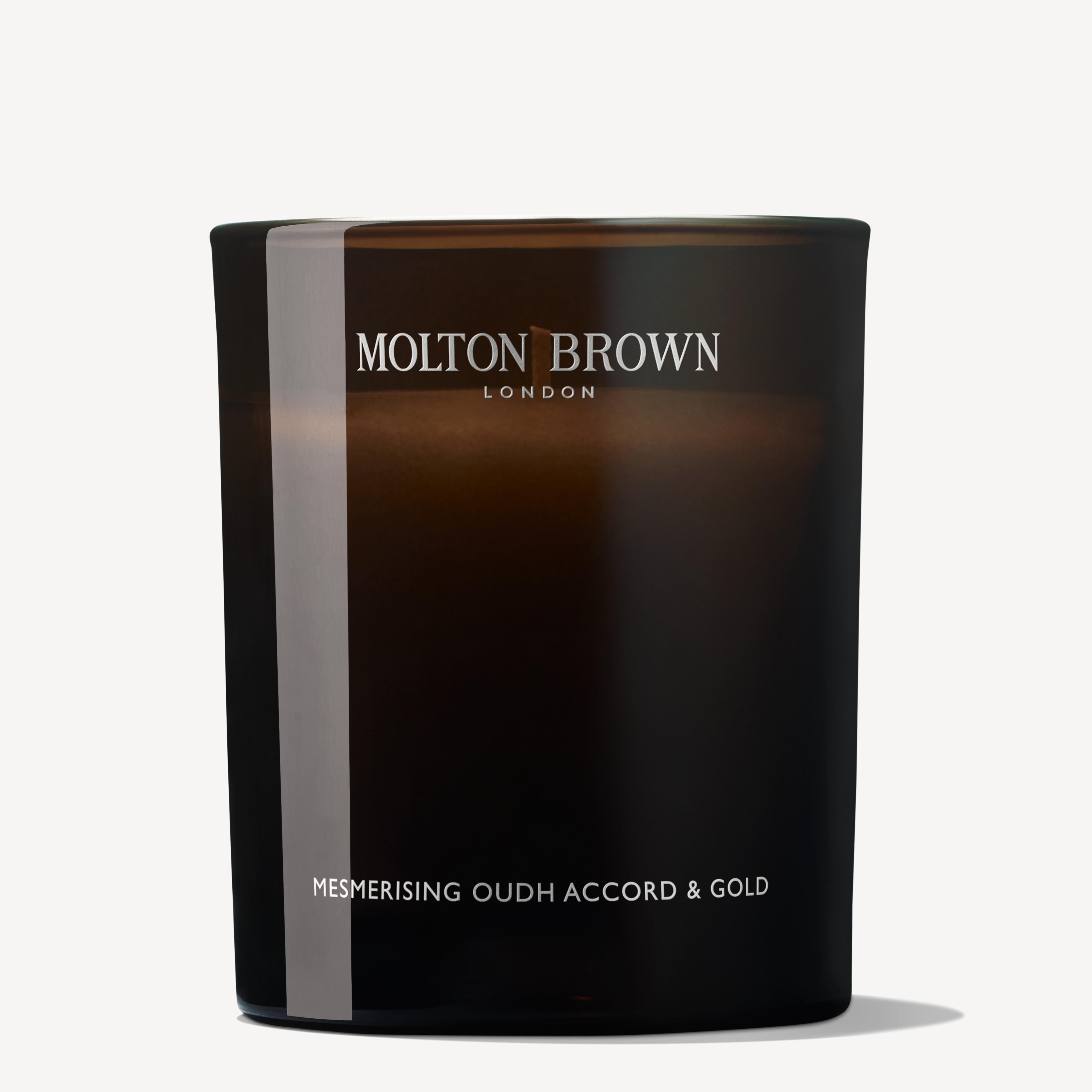 A dark translucent candle labeled MoltonBrown Cyprus, exudes luxury with the Mesmerising Oudh Accord & Gold scent. Hints of oud and cinnamon grace the unlit 190g candle, elegantly set against a plain white background.