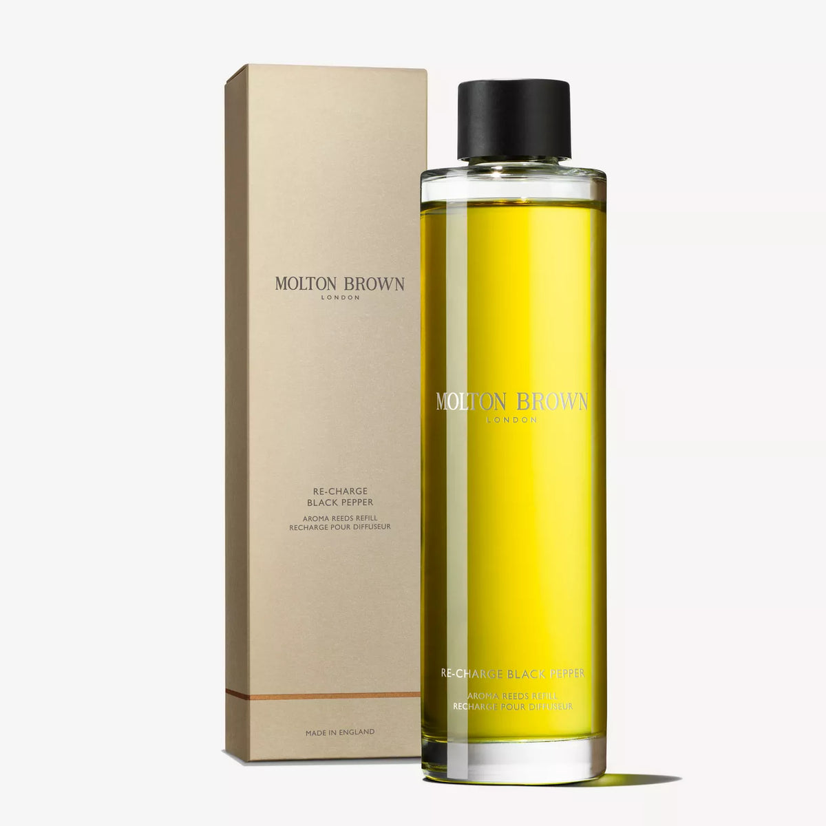 A tall, cylindrical bottle of MoltonBrown Cyprus Re-charge Black Pepper Aroma Reeds Refill 150ml, infused with spices and earthy tones, sits next to its rectangular beige box. The golden-yellow liquid features the brands logo and product details in elegant lettering.