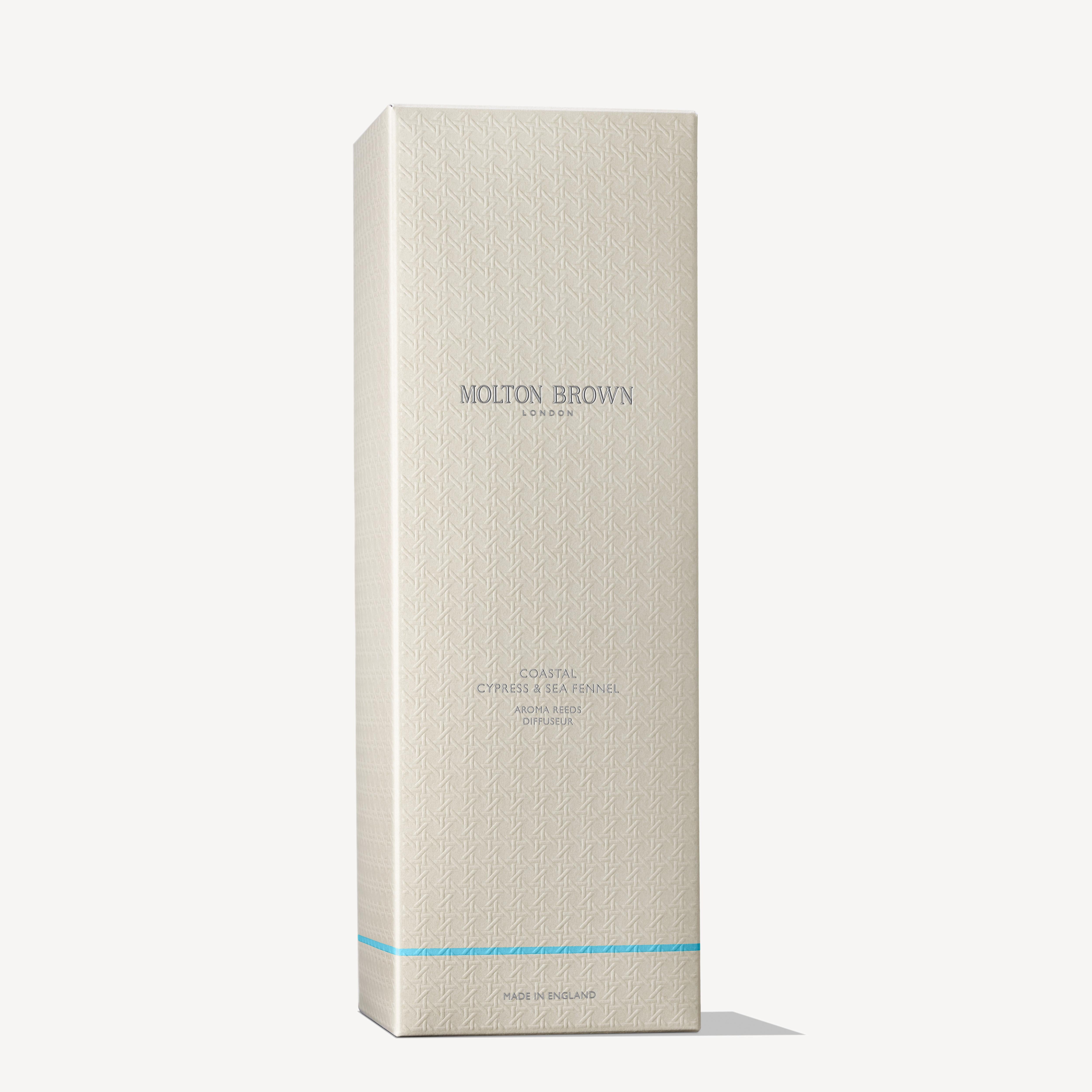 A tall, beige MoltonBrown Cyprus box with blue accents and embossed geometric patterns. The silver text reads Coastal Cypress & Sea Fennel Aroma Reeds 150ml, featuring an aromatic fragrance reminiscent of a sea breeze scent.
