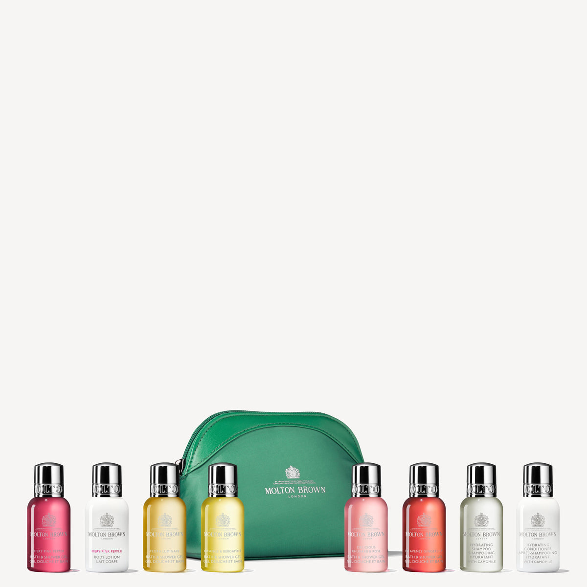 A set of The Elegant Escapist Body & Hair Mini Travel Bag by MoltonBrown Cyprus, showcasing an assortment of travel-size toiletries in vibrant colored bottles, is displayed alongside a green travel bag. This collection includes a variety of fragrances, like refreshing citrus notes, each encased in a small bottle with a shiny cap.