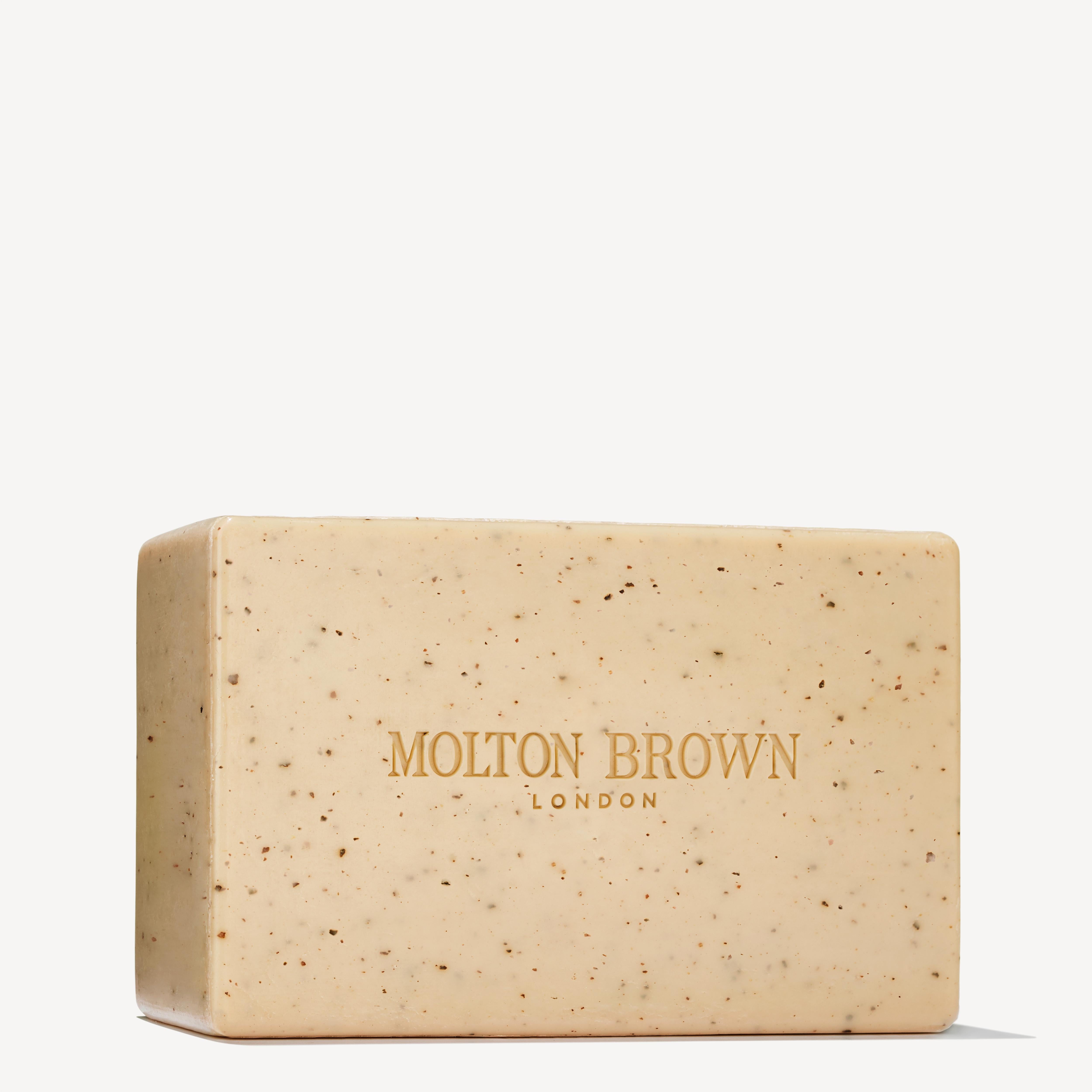 A beige rectangular Re-charge Black Pepper Bodyscrub Bar by MoltonBrown Cyprus features a speckled texture and is infused with Madagascan black peppercorn oil. The soap, smoothly embossed with the brand's name in gold lettering, is displayed against a plain white background.