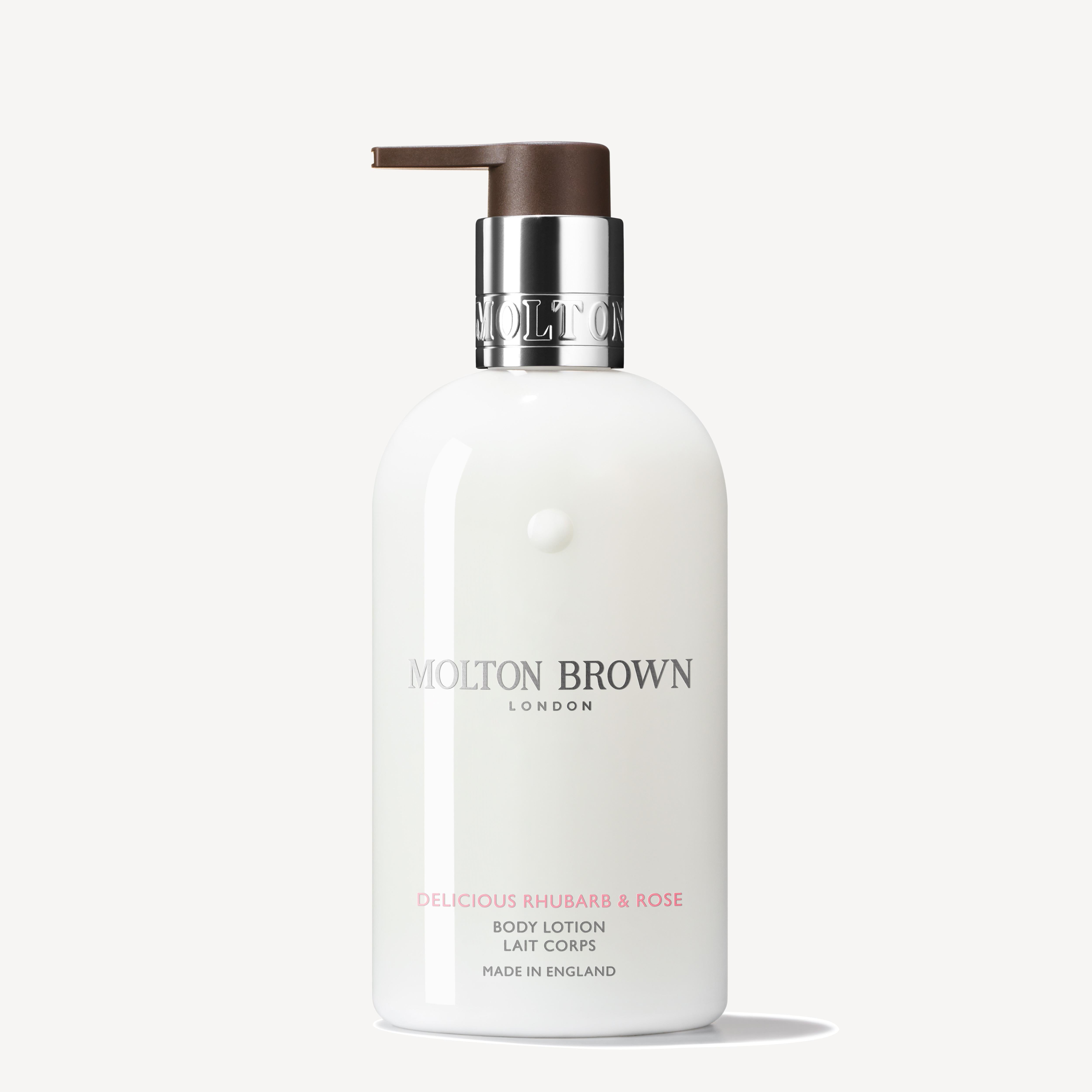 A 300ml bottle of MoltonBrown Cyprus Delicious Rhubarb & Rose Body Lotion with a pump dispenser offers an enchanting fragrance. The elegant white bottle adorned with silver and brown accents, labeled "Made in England," adds a luxurious touch to your skincare routine.