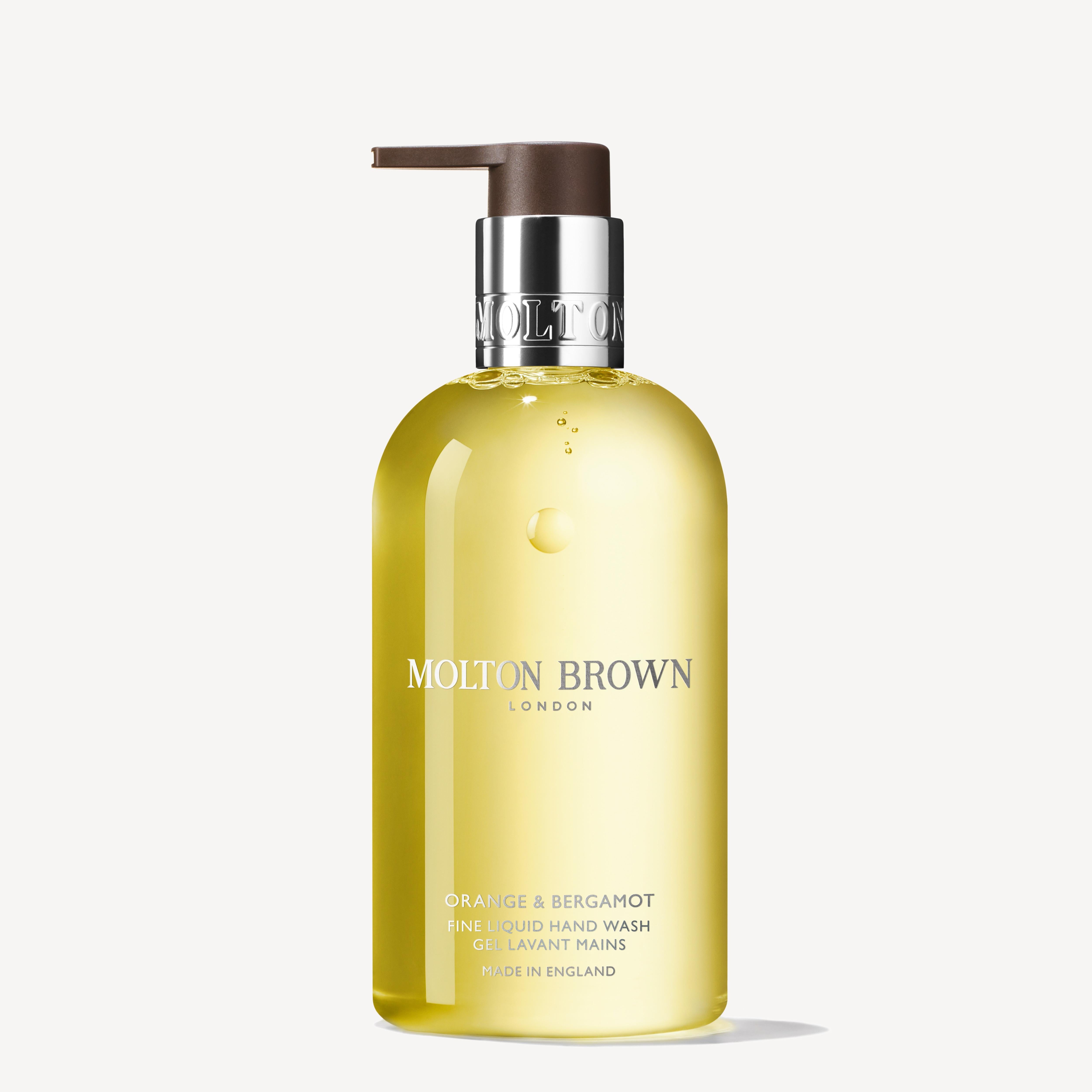 The Orange & Bergamot Fine Liquid Hand Wash 300ml by MoltonBrown Cyprus comes in a clear pump bottle showcasing a pale yellow liquid infused with neroli. The label features silver text, while the brown pump contributes to its elegance. This exquisite product is proudly made in England.