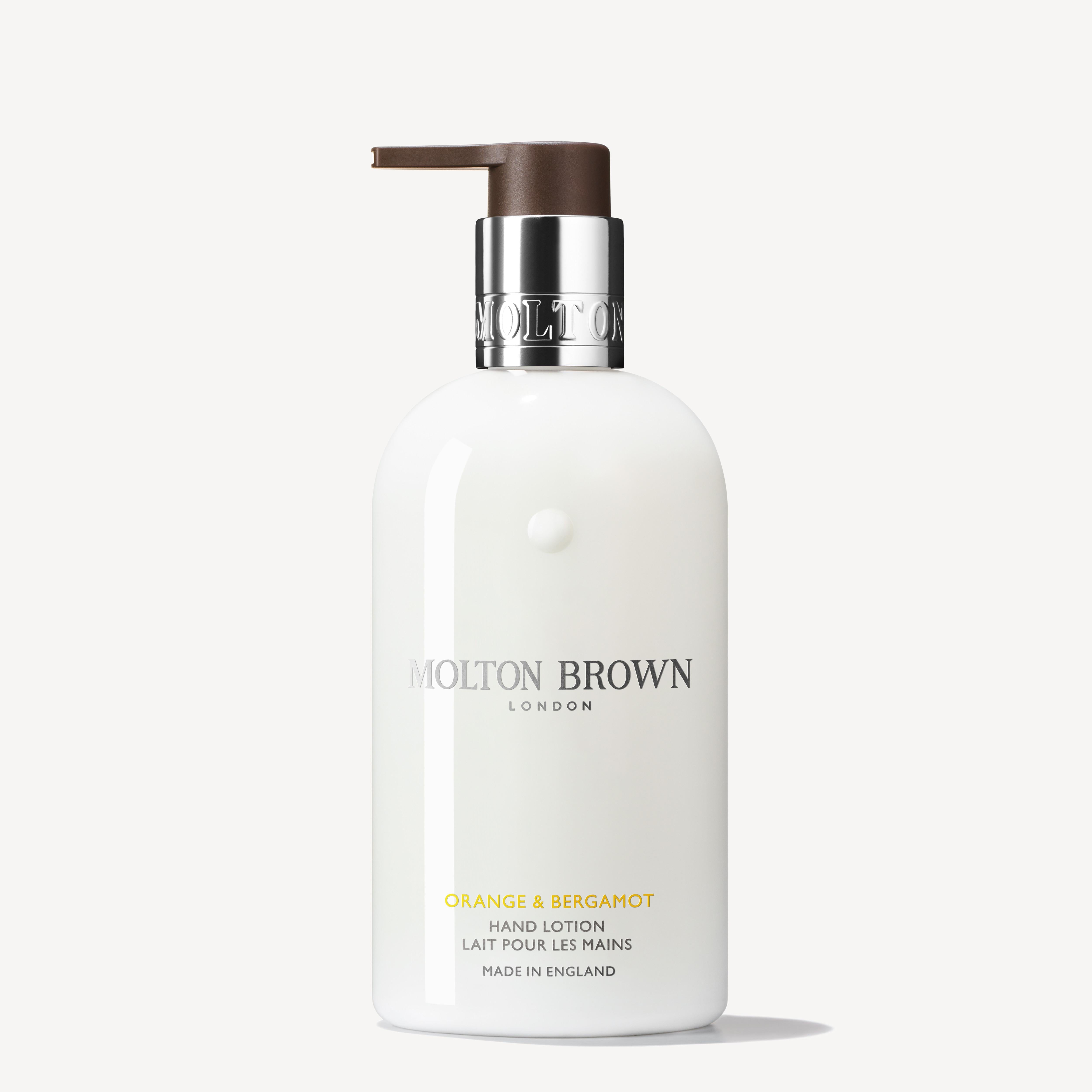 A 300ml bottle of MoltonBrown Cyprus Orange & Bergamot Hand Lotion, infused with the essence of neroli, showcases a brown pump and silver collar with the brand's logo. The label prominently features "London" and "Made in England," set against a crisp white backdrop.