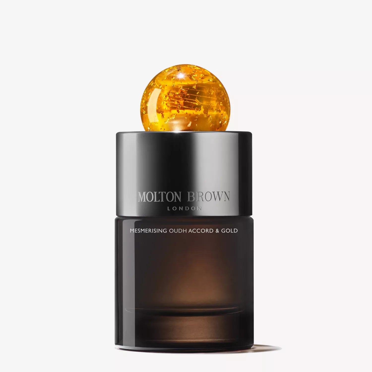A sleek, dark collectible glass flacon of Mesmerising Oudh Accord & Gold Eau de Parfum 100ml by MoltonBrown Cyprus, topped with a shiny spherical golden cap, stands elegantly against a white background.