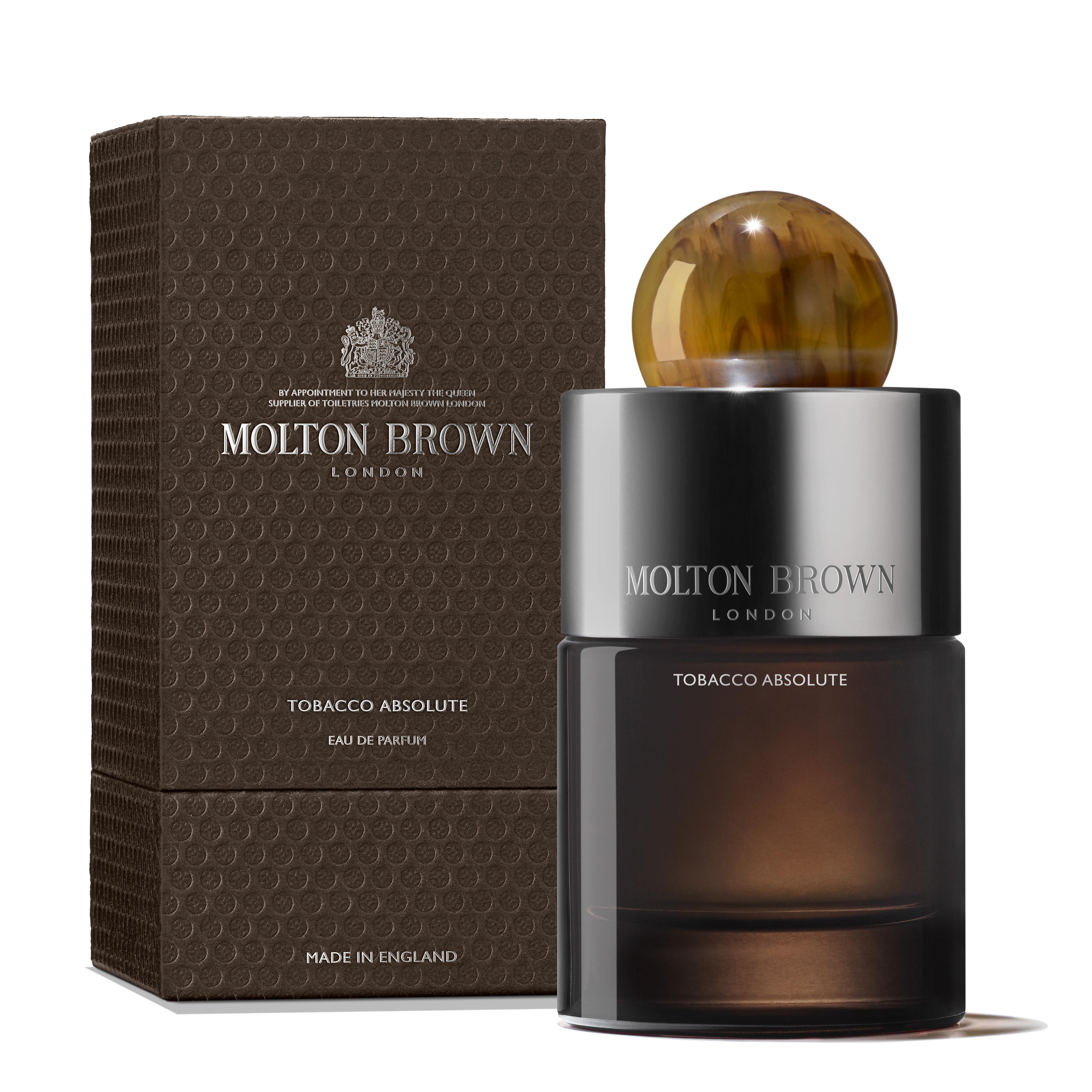 A MoltonBrown Cyprus Eau de Parfum bottle labeled Tobacco Absolute stands beside its textured brown box. The bottle is dark with a spherical, marbled cap. Both the bottle and box display the brand and fragrance name in elegant lettering, capturing the essence of a woody fragrance with smoky tobacco notes.