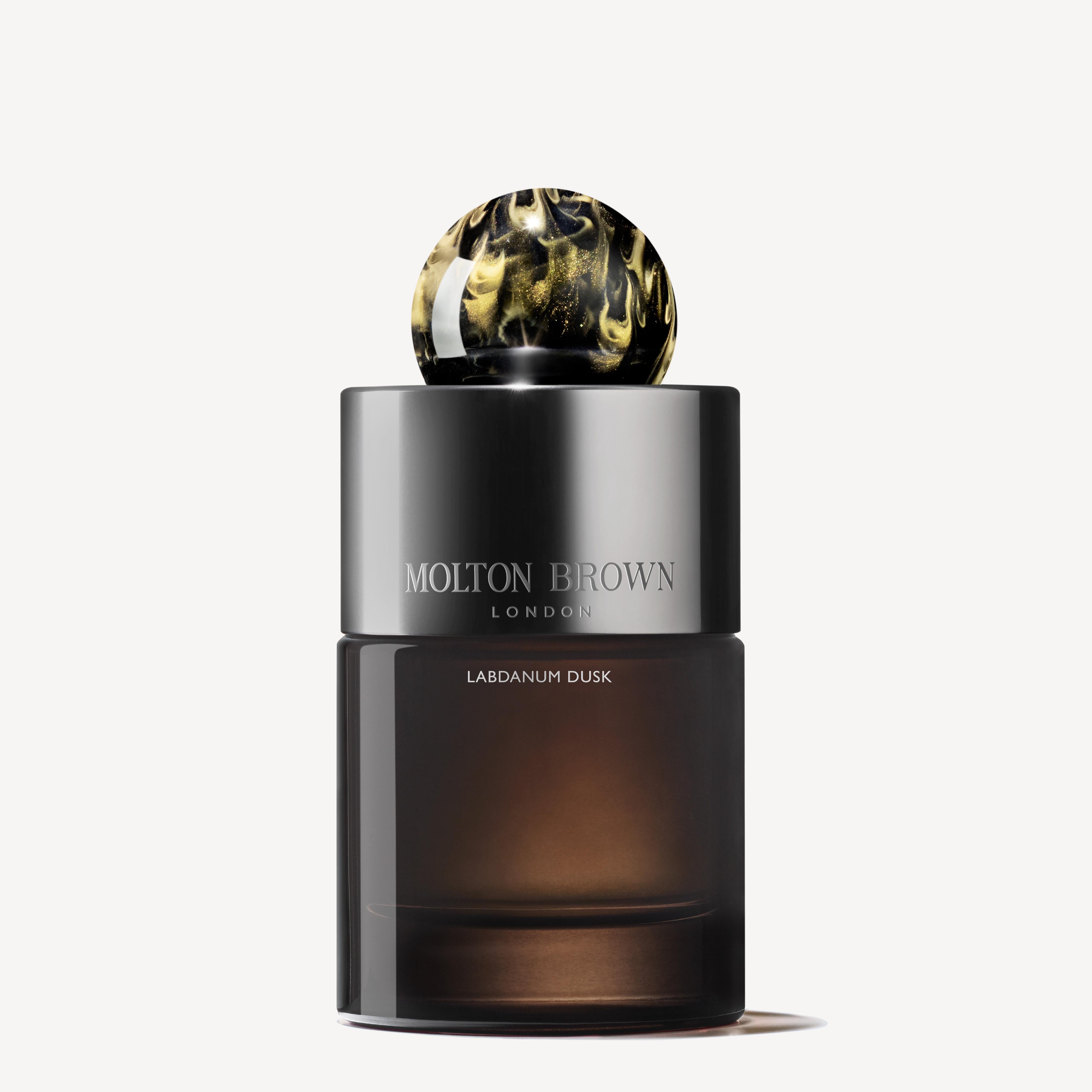 A bottle of Labdanum Dusk Eau de Parfum 100ml by MoltonBrown Cyprus features a dark, glossy design with a decorative marbled spherical cap. It captures an amber woody essence with its rare oudh scent, offering a luxurious fragrance experience against the off-white background.