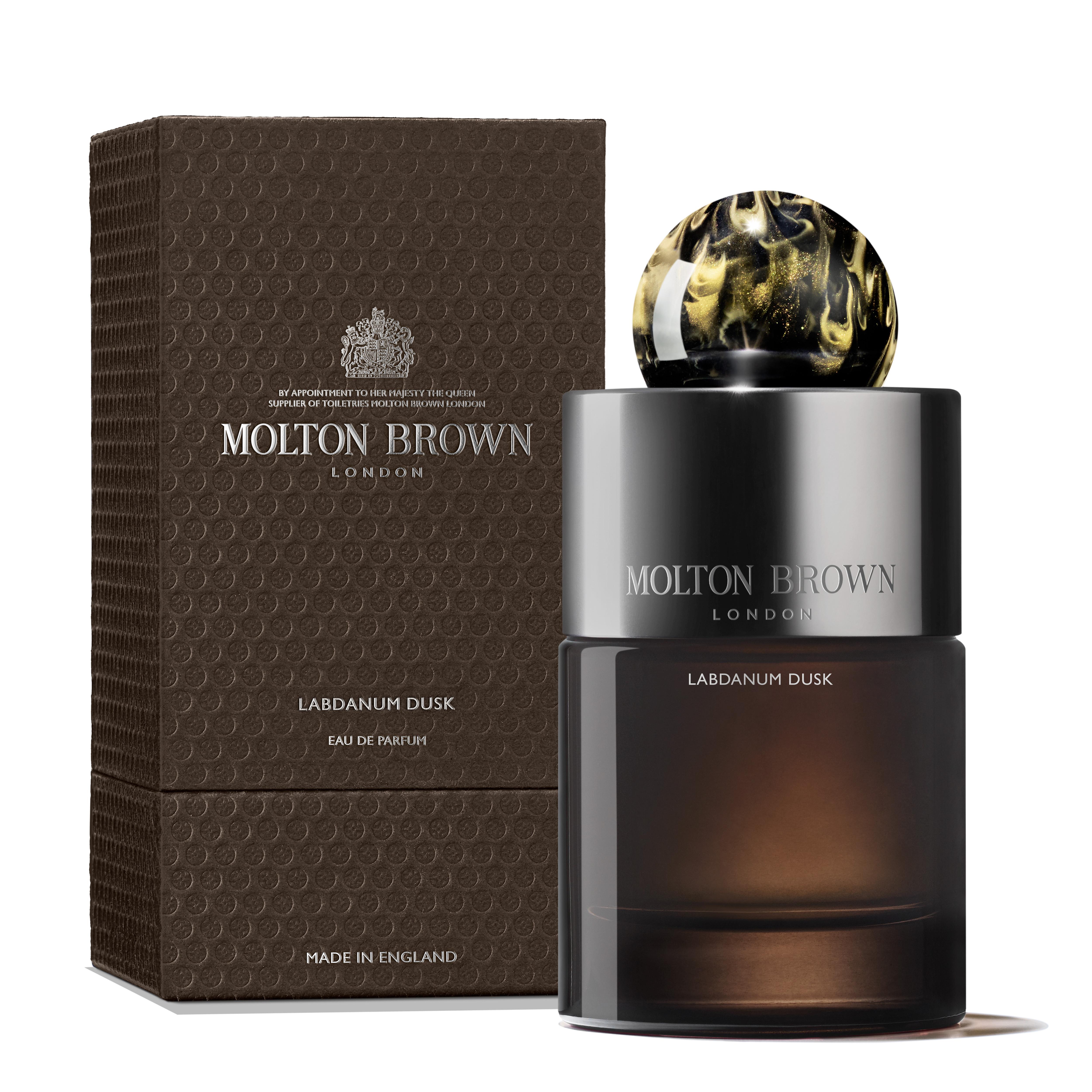 A bottle of Labdanum Dusk Eau de Parfum 100ml by MoltonBrown Cyprus stands next to its textured, dark brown packaging. The sleek black and gold design, highlighted by a round marbled cap, exudes an amber woody elegance. The words MoltonBrown Cyprus shimmer on both the box and bottle.