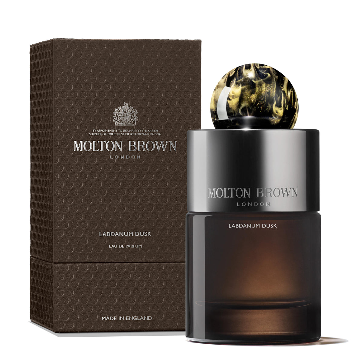 A bottle of Labdanum Dusk Eau de Parfum 100ml by MoltonBrown Cyprus stands next to its textured, dark brown packaging. The sleek black and gold design, highlighted by a round marbled cap, exudes an amber woody elegance. The words MoltonBrown Cyprus shimmer on both the box and bottle.