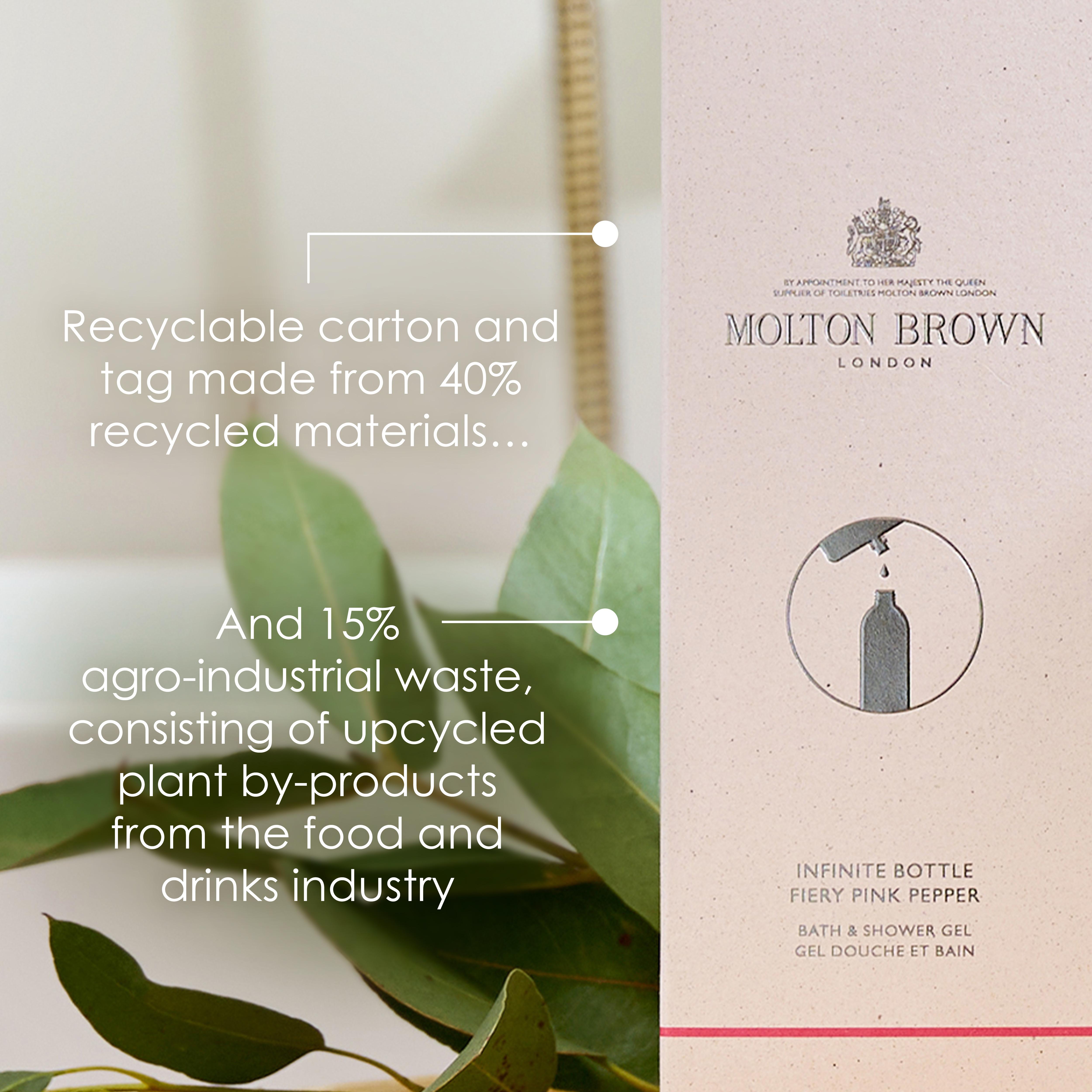A MoltonBrown Cyprus Fiery Pink Pepper Infinite Bottle 400ml, crafted from recycled aluminium, is presented next to its packaging box made of recycled materials. The display emphasizes its eco-friendly attributes, boasting 40% recycled content and 15% agro-industrial waste utilization. Partially visible green leaves in the background reflect a dedication to sustainability.