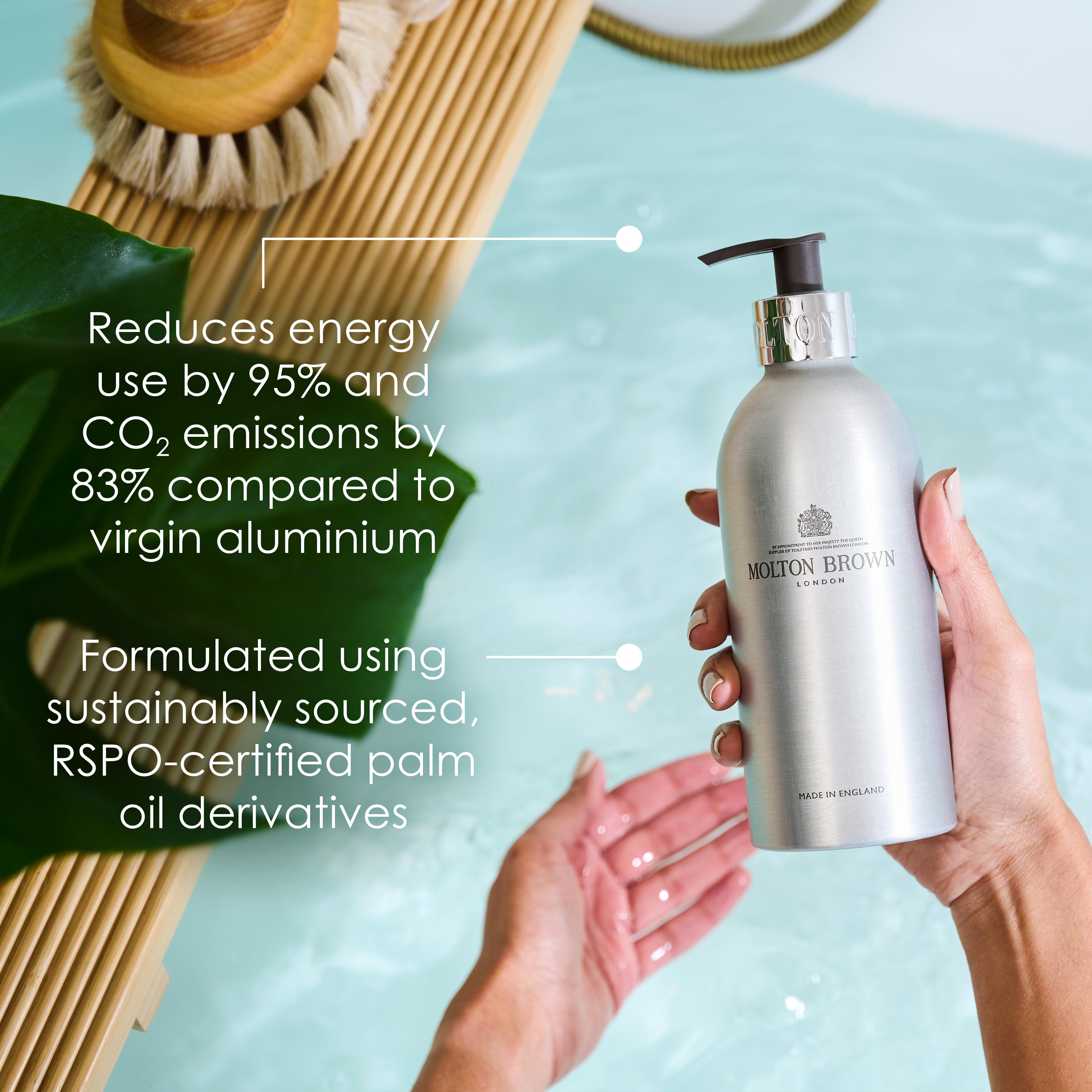 A person holds a MoltonBrown Cyprus Re-charge Black Pepper Infinite Bottle 400ml, featuring a woody-citrus body wash in a recycled aluminum bottle, over a bathtub filled with water. The text highlights benefits such as a 95% reduction in energy use and CO2 emissions, along with the formulation that includes sustainably sourced RSPO-certified palm oil derivatives.
