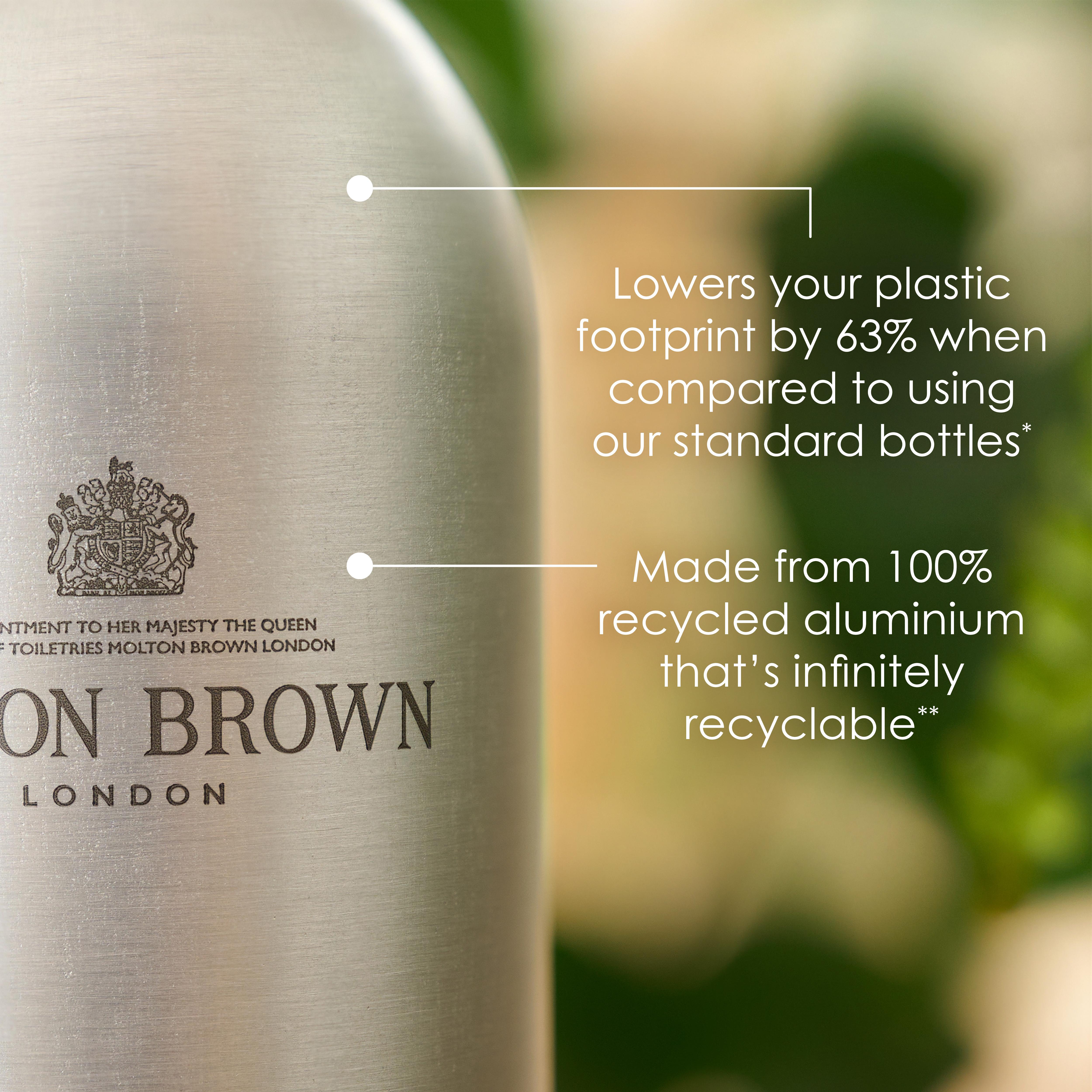 A close-up of the Coastal Cypress & Sea Fennel Infinite Bottle 400ml, a sleek silver bottle by MoltonBrown Cyprus, crafted from 100% recycled aluminum, proudly showcases its contribution to a sustainable bathing routine. This Bath & Shower Gel reduces the plastic footprint by 63% compared to standard bottles. Its eco-friendly appeal is complemented by a blurred green background.