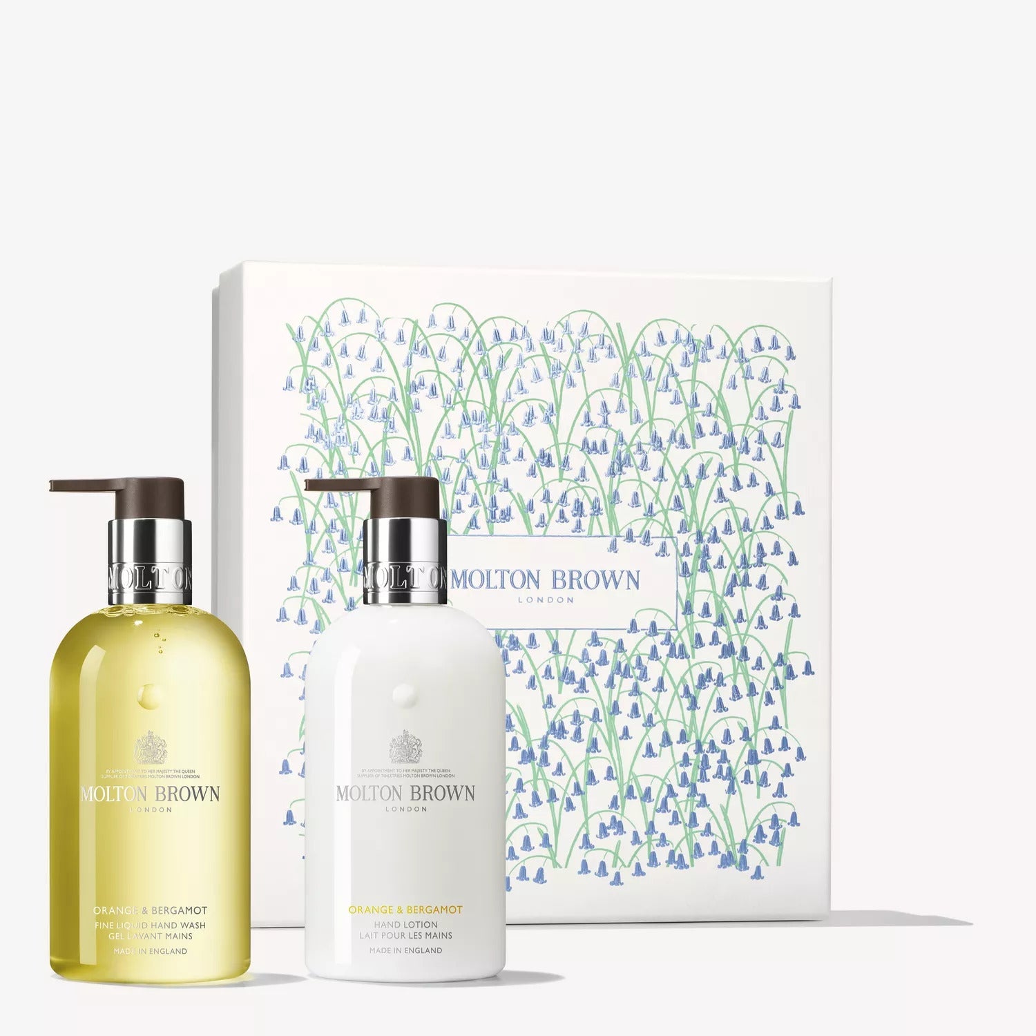 Two bottles from the MoltonBrown Cyprus Orange & Bergamot Hand Care Gift Set, one with citrus-infused yellow shower gel and the other with creamy white body lotion, sit elegantly in front of a decorative box adorned with blue flowers and green stems.