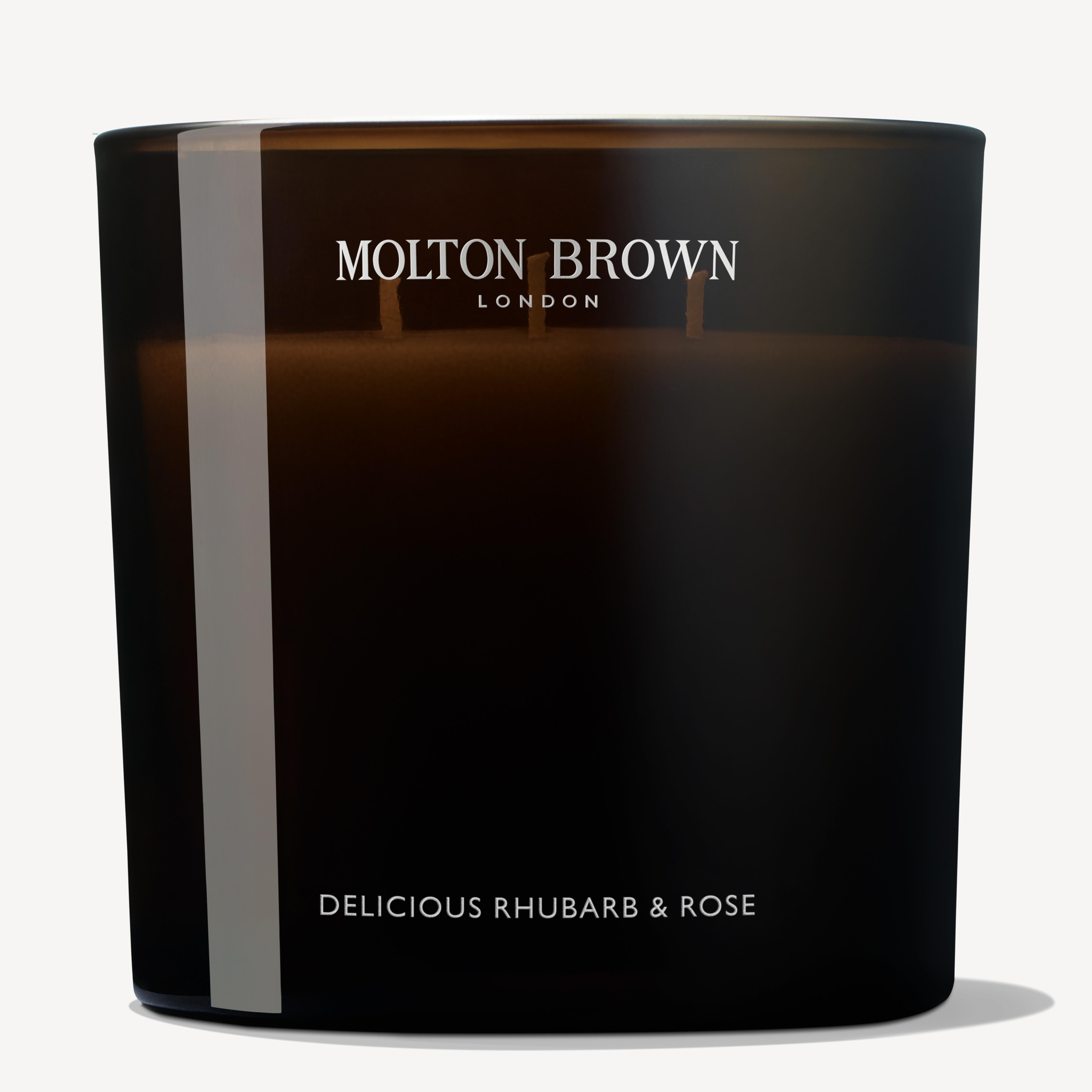 A Delicious Rhubarb & Rose Luxury Candle by MoltonBrown Cyprus, encased in a dark glass container, offers an unlit floral-fruity essence with notes of grapefruit and features the brand name elegantly displayed at the top.