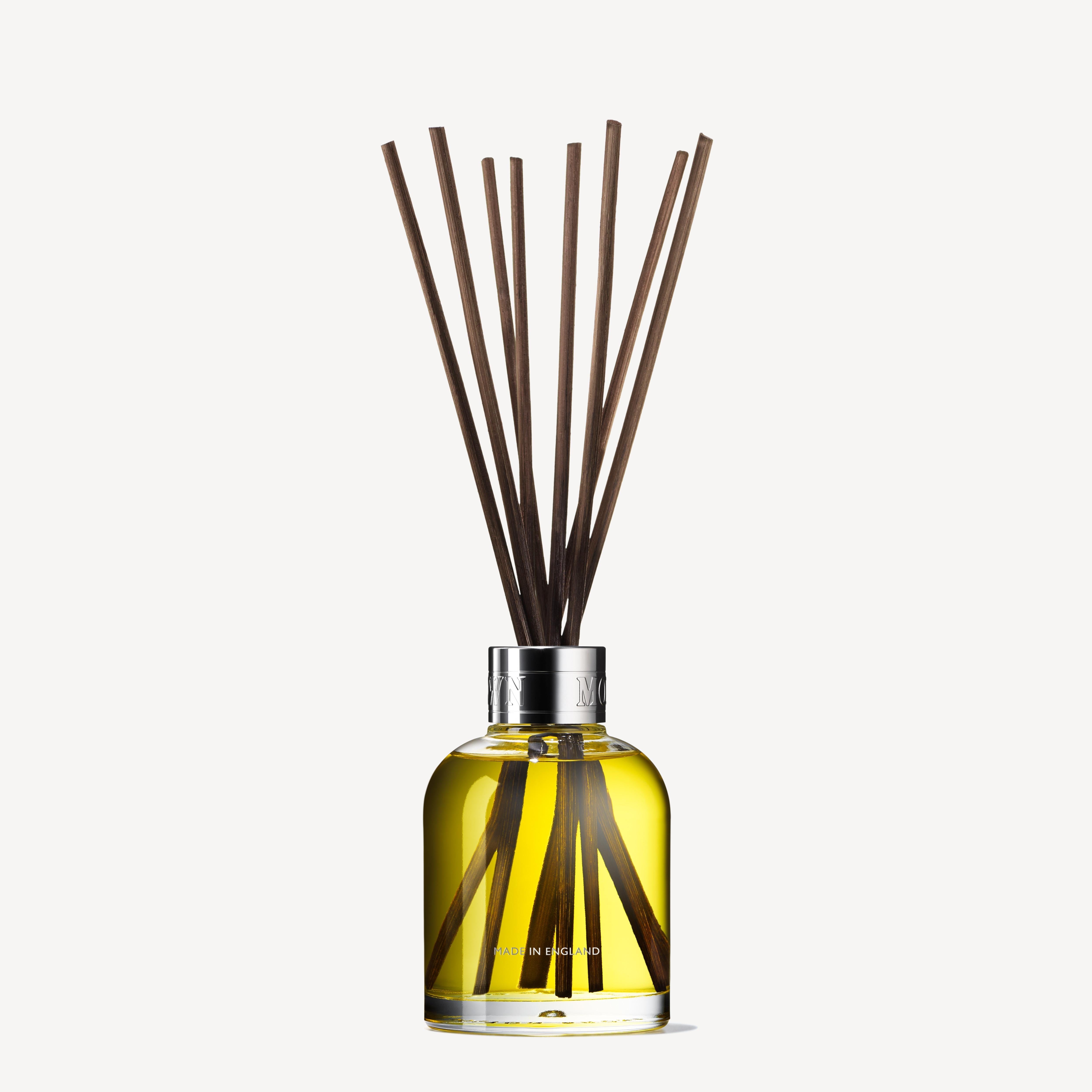 A Coastal Cypress & Sea Fennel Aroma Reeds set from MoltonBrown Cyprus, featuring a glass diffuser bottle filled with aromatic yellow liquid and topped with several brown aroma reeds, is displayed against a plain light background.