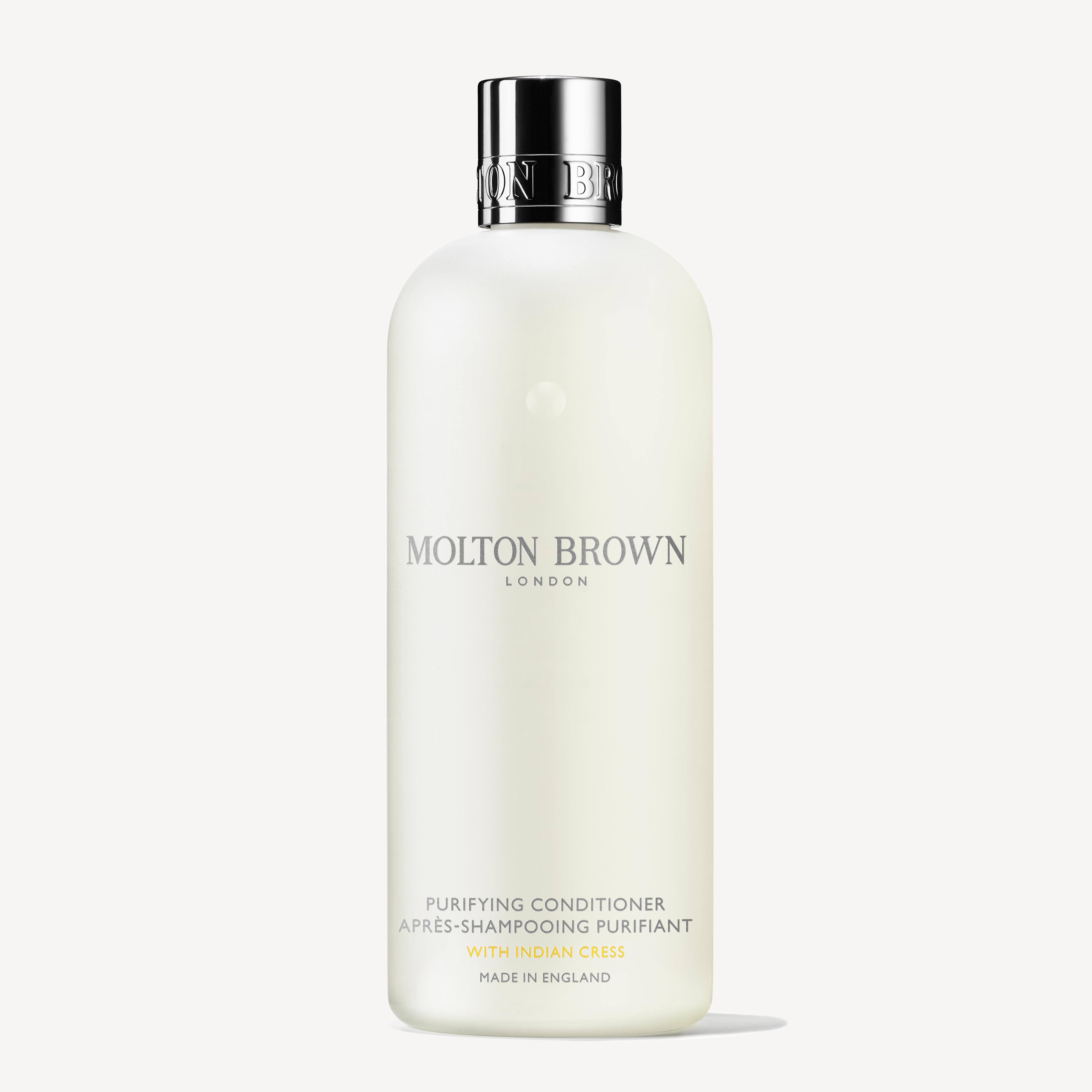 A white bottle of Molton Brown Cyprus Purifying Conditioner With Indian Cress 300ml is displayed. The text on the bottle features LONDON and Made in England in elegant fonts, with a simple, sleek design that exudes sophistication and is enhanced by subtle notes of honeysuckle.