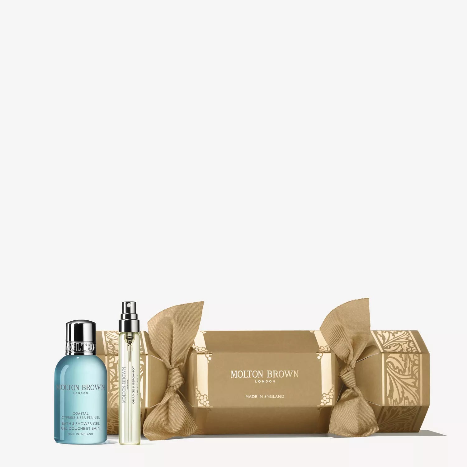 The Coastal Cypress & Sea Fennel Christmas Cracker by MoltonBrown Cyprus is shown with a blue shower gel bottle and a slim travel fragrance spray beside it.