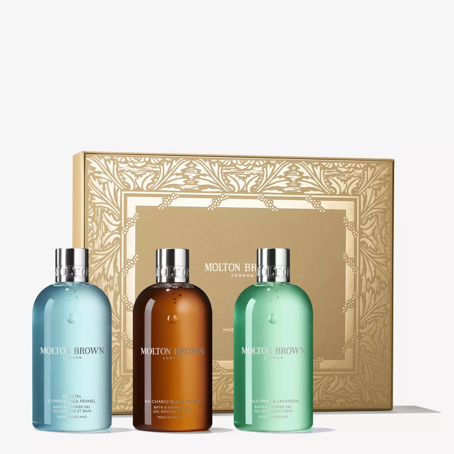 The Woody & Fresh Body Care Gift Set by MoltonBrown Cyprus features three bath & shower gels in blue, amber, and green, displayed before an ornate gold gift box, promising a luxurious sensory experience.