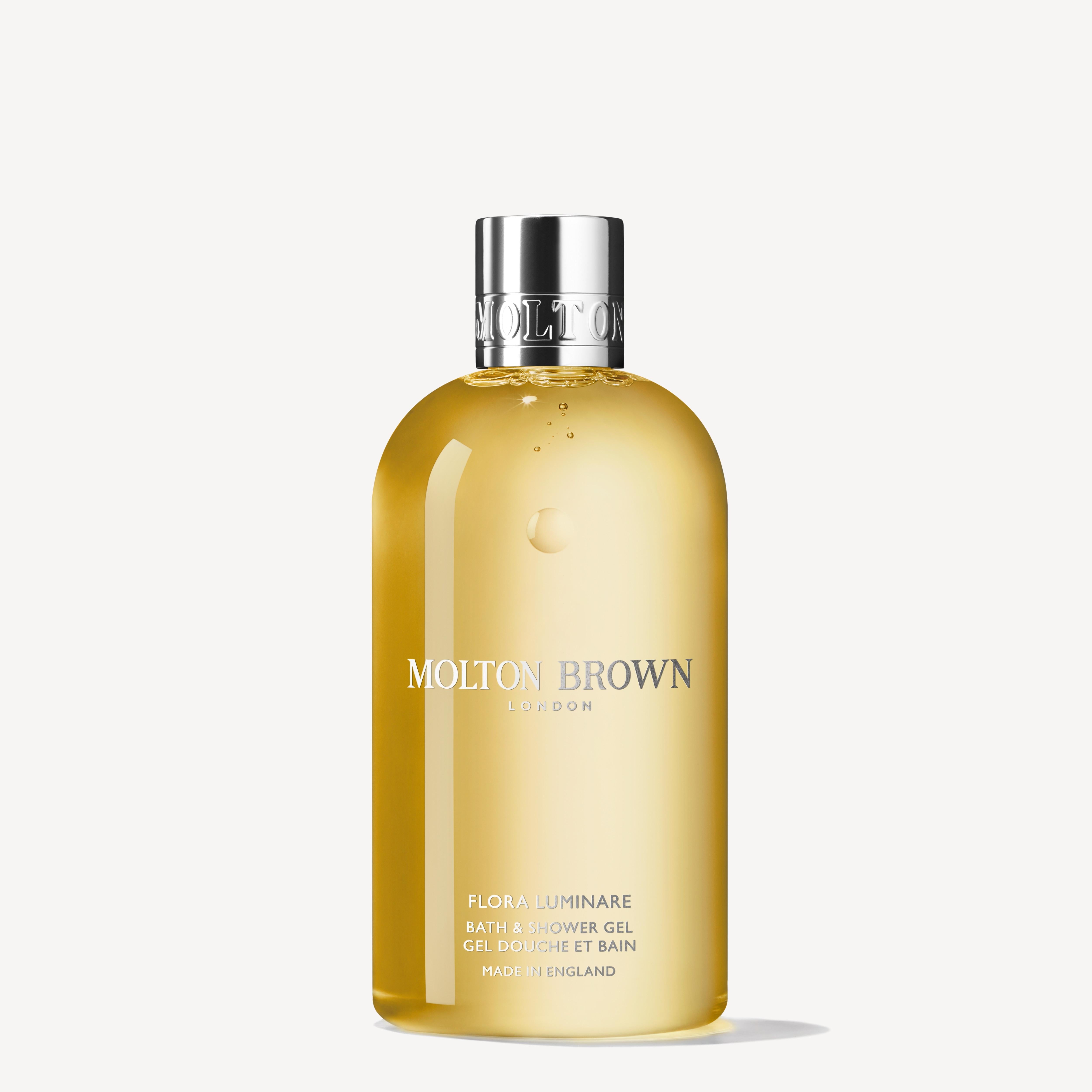 A 300ml bottle of MoltonBrown Cyprus Flora Luminare Bath & Shower Gel emanates a floral essence with notes of orange blossom. Its transparent design showcases the vibrant yellow liquid within, crowned by a silver cap that elegantly displays the brand's name and product details on the front.