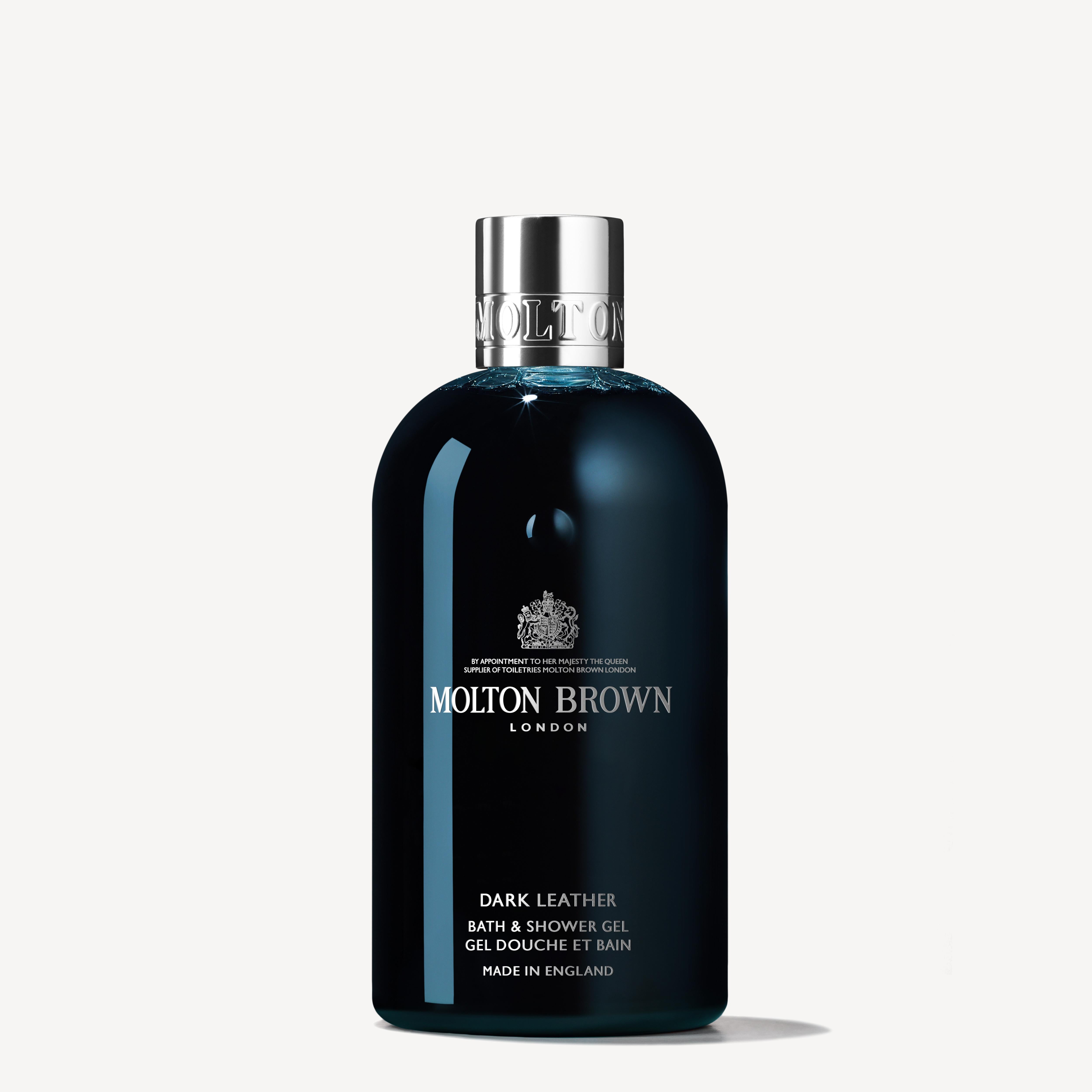 A 300ml bottle of MoltonBrown Cyprus Dark Leather Bath & Shower Gel, featuring a chrome cap, exudes sophistication. Its black label with white text prominently displays the brand's logo and product details, while notes of aged leather and a subtle tobacco accord enhance this luxurious experience against an off-white backdrop.