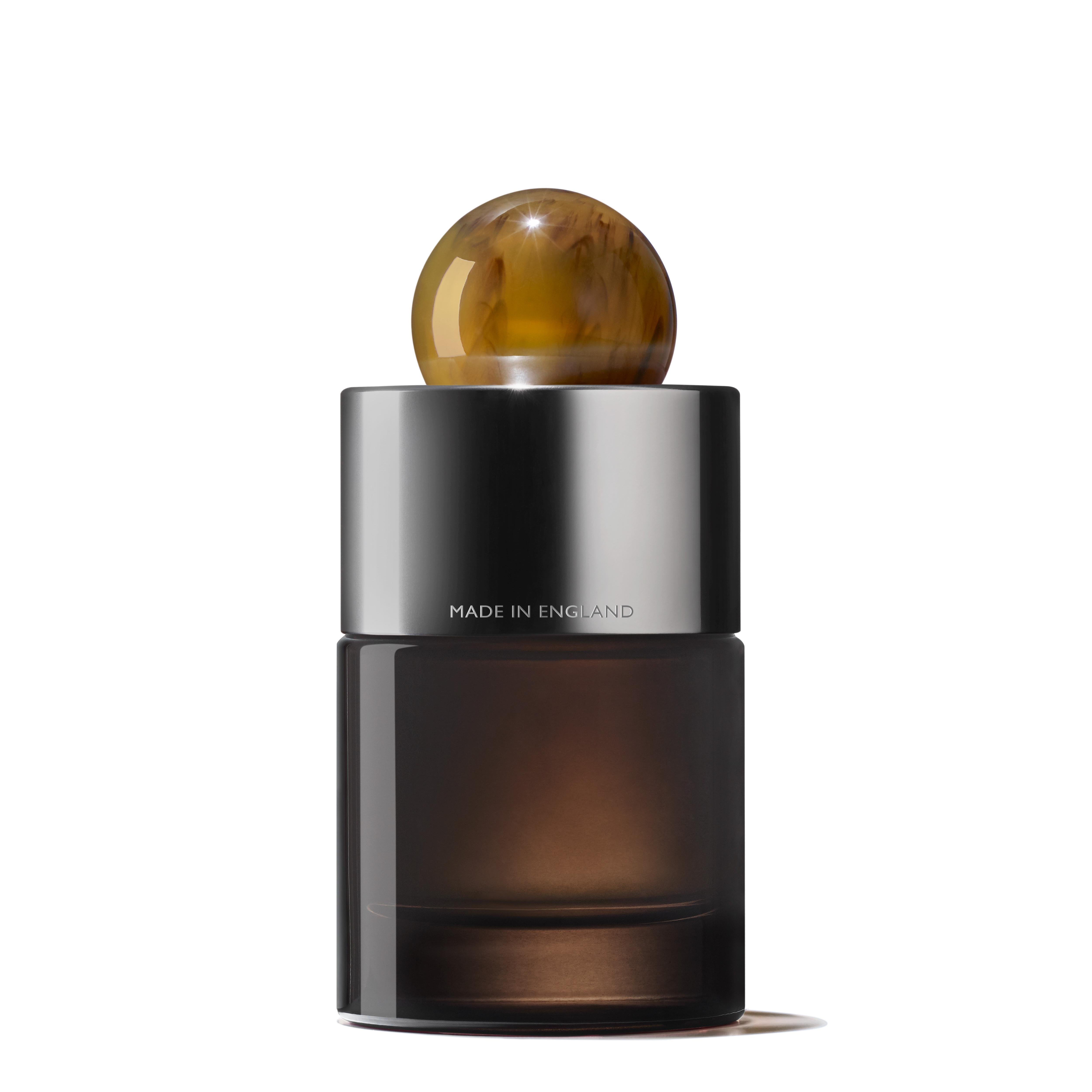 The Tobacco Absolute Eau de Parfum 100ml by MoltonBrown Cyprus features a modern design with a dark, cylindrical base and a shiny, metallic cap. A marbled, spherical stopper sits atop the bottle, which reads MADE IN ENGLAND. This sleek perfume bottle encases an Eau de Parfum infused with woody fragrance notes and hints of smoky tobacco for an elegant allure.